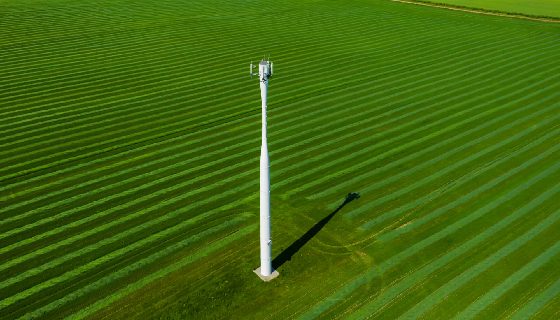 Aerial view of a sleek white monopole cellular tower in a green landscape